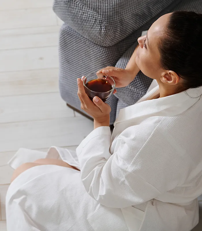 attractive-brunette-woman-white-bathrobe-sitting-floor-leaning-sofa-with-cup-coffee-hands